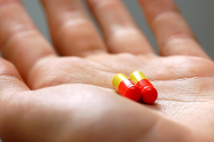 Hand holding two capsules; person can't get off medication treadmill