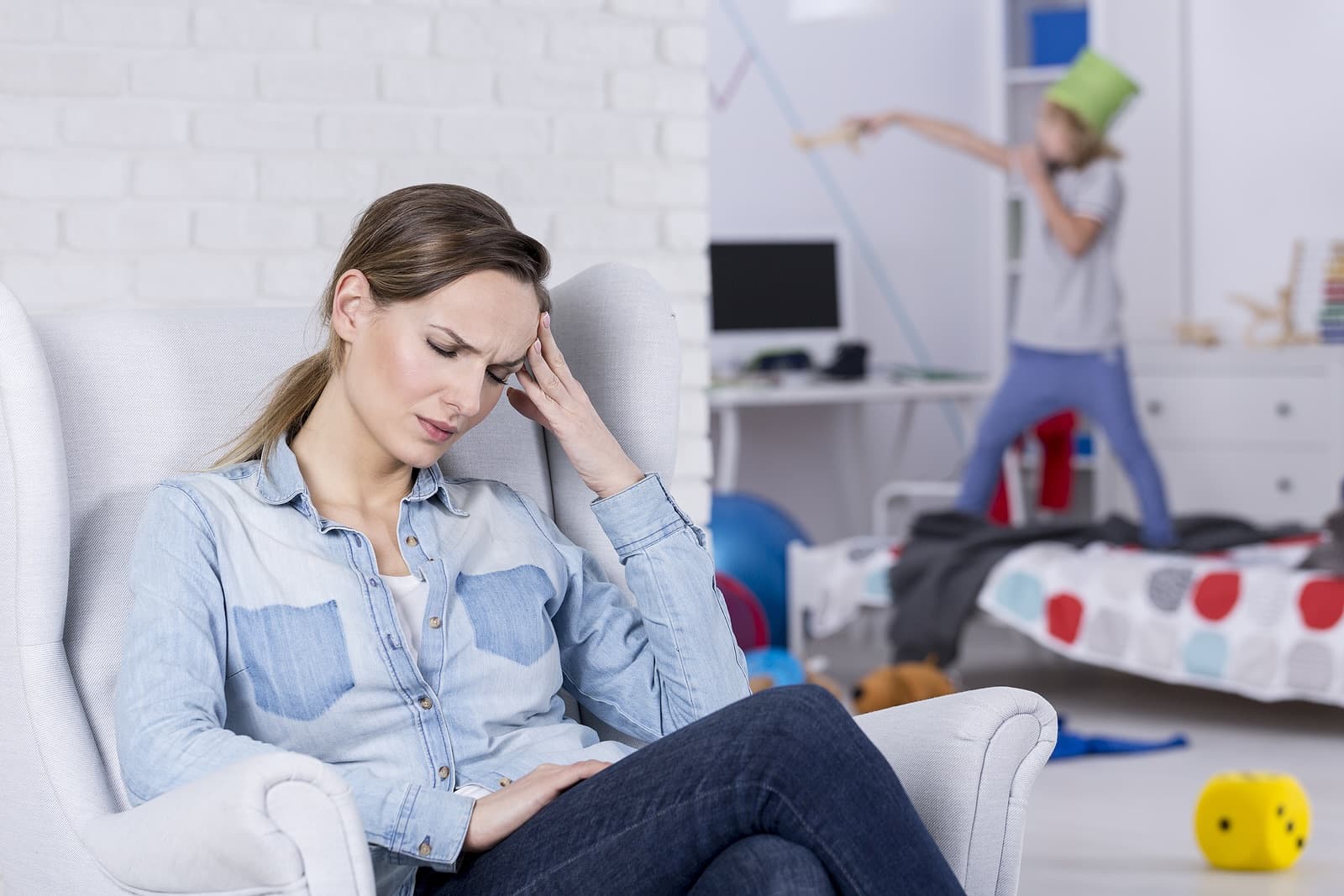 Mother in foreground looks defeated, child climbing over bed in background; what we get wrong about ADHD