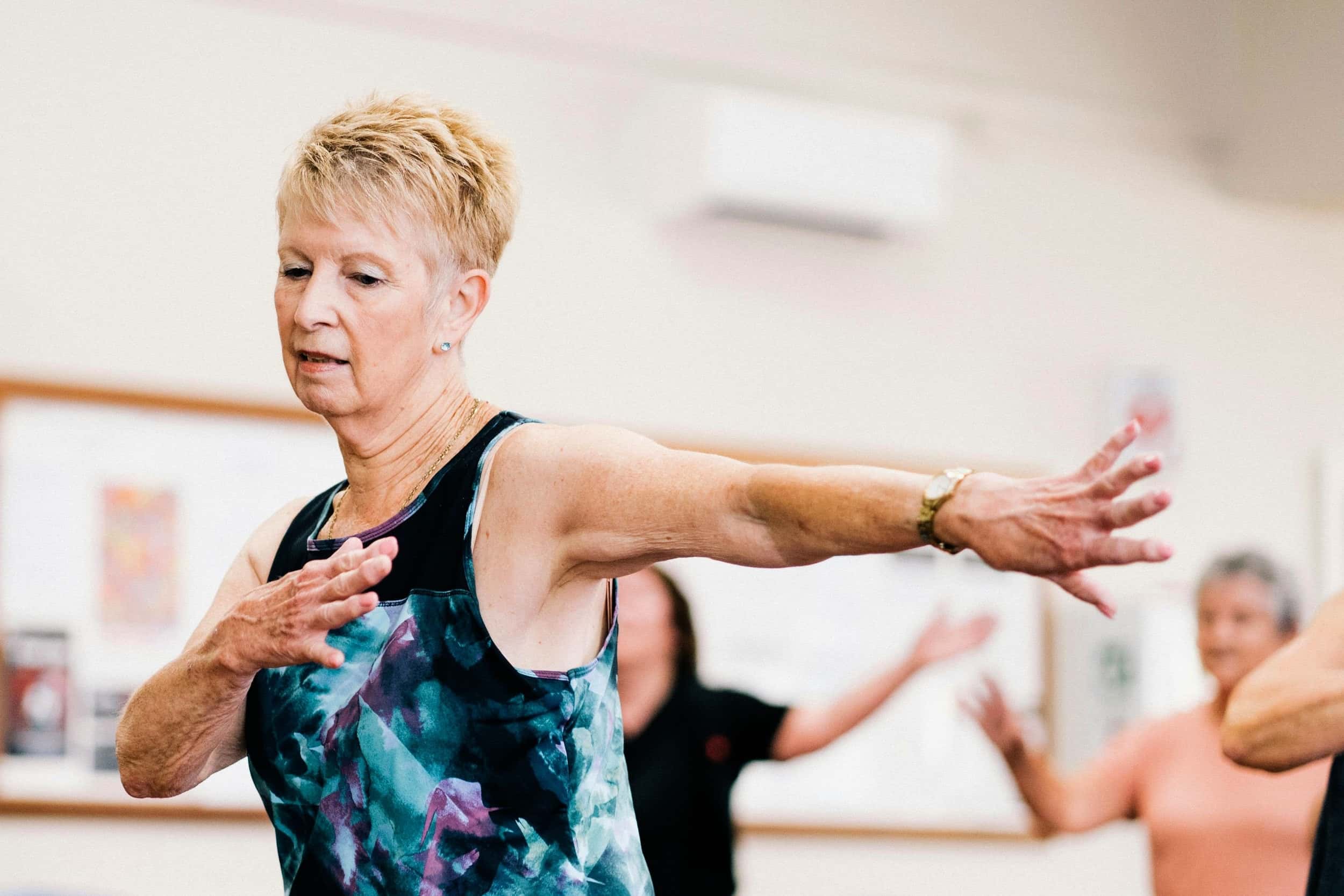 Older woman in an exercise class extending her arms sideways during a group fitness dance class.